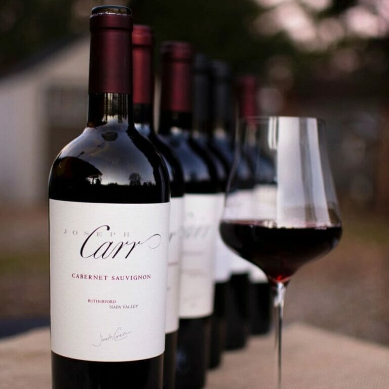 red wine glass standing beside of line of carr cabernet sauvignon bottles