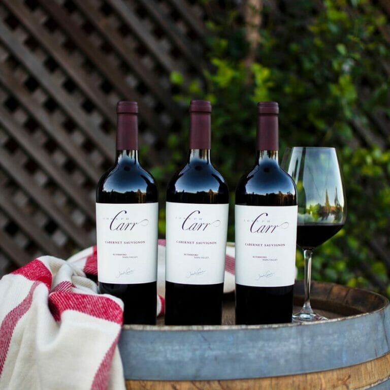 three bottles of rutherford cabernet sauvignon, wine glass and towel sitting on barrel