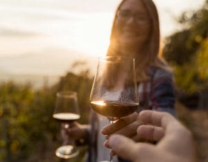 hand reaching out to woman holding two glasses of red wine outside on sunny day