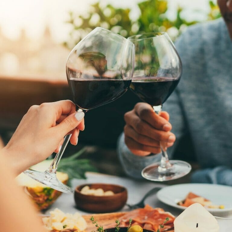 man and woman clinking glasses of cabernet sauvignon red wine together at table with food